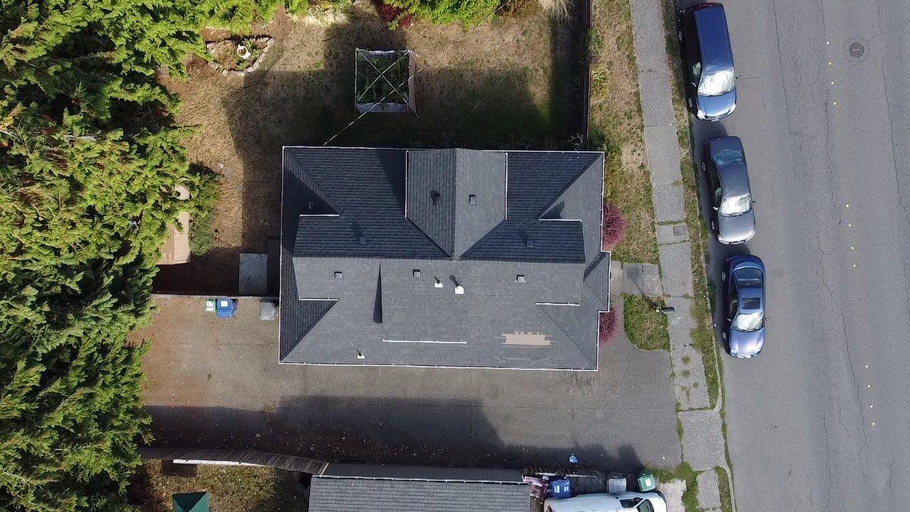 Picture from above. Shingles roof replacement before. It has blown off shingles and is a black worn out roof.