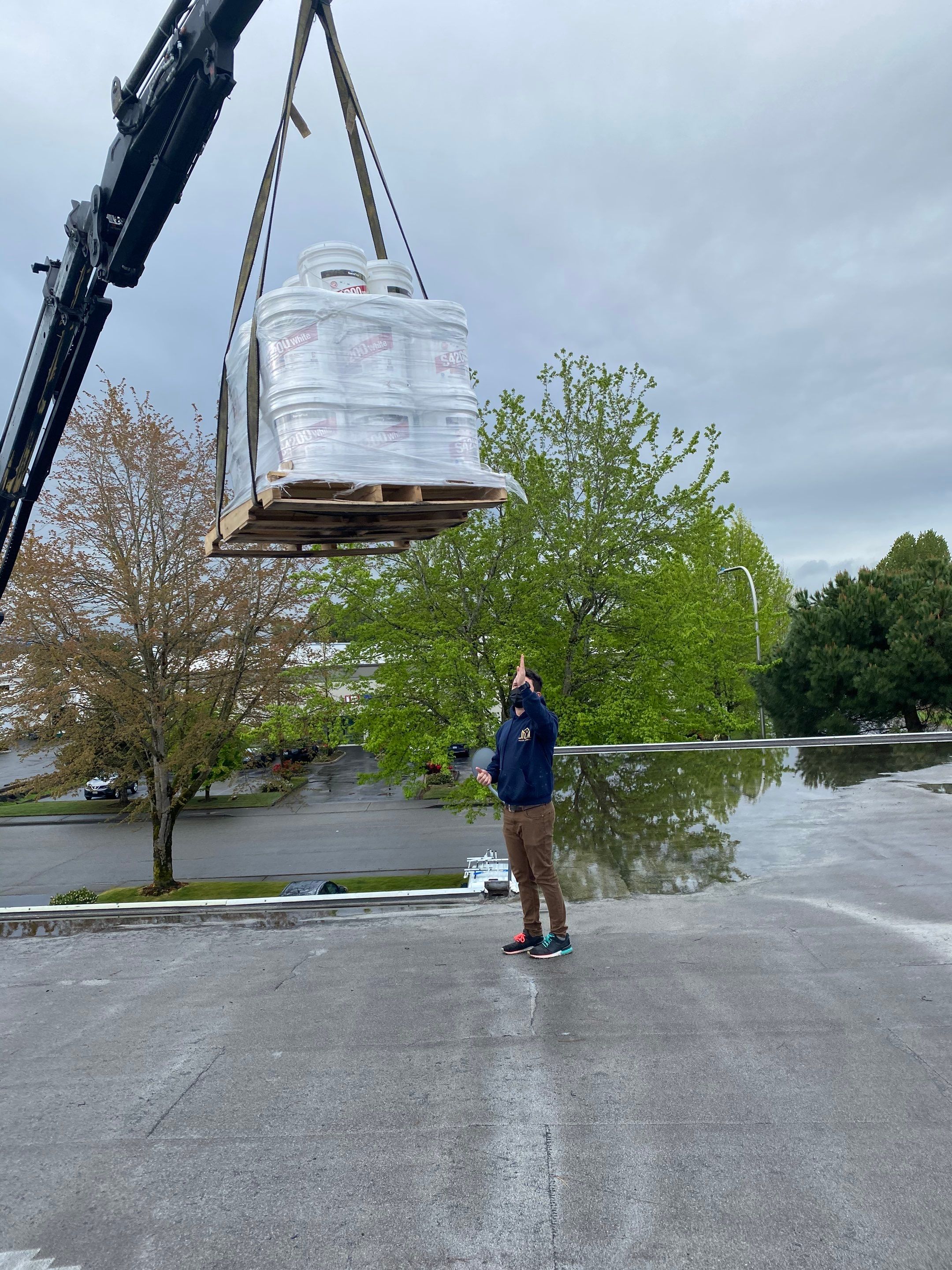 A skilled roofer is seen directing a boom lift to place materials onto a commercial roof during a roofing project, demonstrating the coordination and efficiency of Trade Roofing's services.