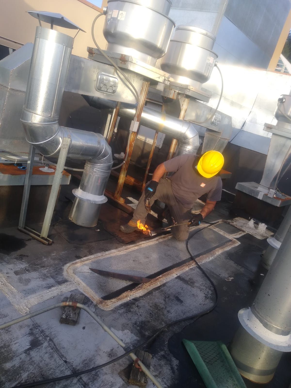 A Roofer is kneeling on a commercial roof, carefully torching down a patch. This expert repair work is ensuring the longevity and performance of the roof.